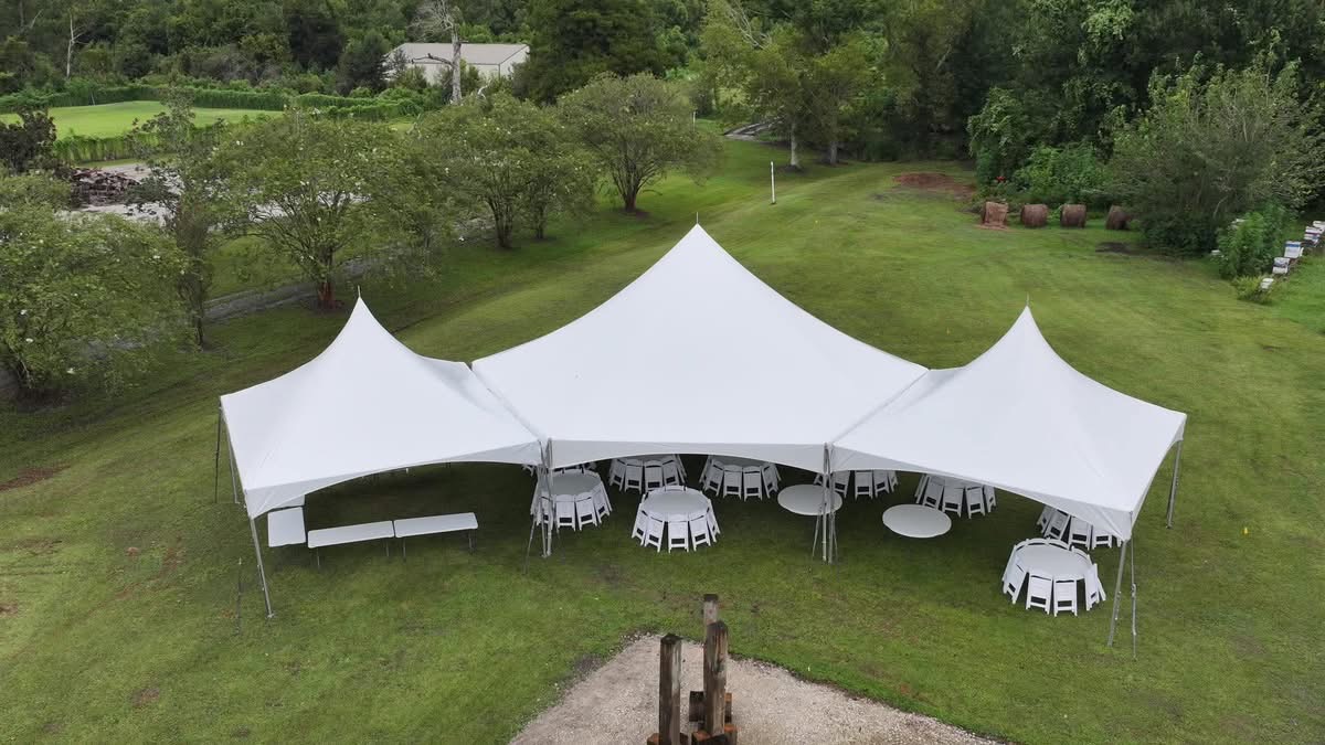 Large pole tent set up on a lawn with round tables and chairs